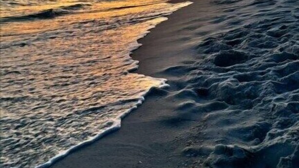Ein Strand bei Sonnenuntergang, mit Wellen.