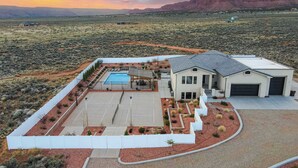Et moderne hus med swimmingpool, omgivet af en indhegnet have, beliggende i et ørkenlandskab med bjerge i baggrunden.