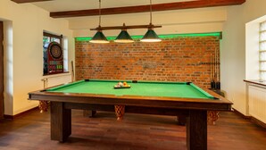 Una mesa de billar en una sala con vigas de madera a la vista, pared de ladrillo y dardo.