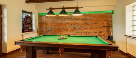 A pool table in a room with exposed wooden beams, a brick wall, and a dartboard.