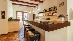Zona de bar con una barra larga, varios taburetes y una pared llena de botellas de licor.