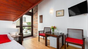 Una habitación con cama, escritorio, dos sillas, un refrigerador pequeño y un televisor montado en la pared.