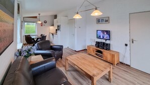 Een moderne woonkamer met een houten salontafel, een zwarte leren bank en een tv op een houten dressoir.