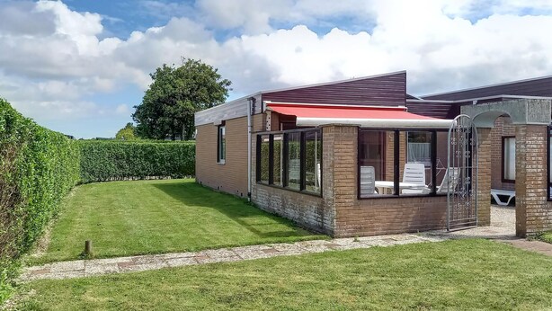 Een huis met een overdekte patio, een verzorgd gazon en een grote boom op de achtergrond.