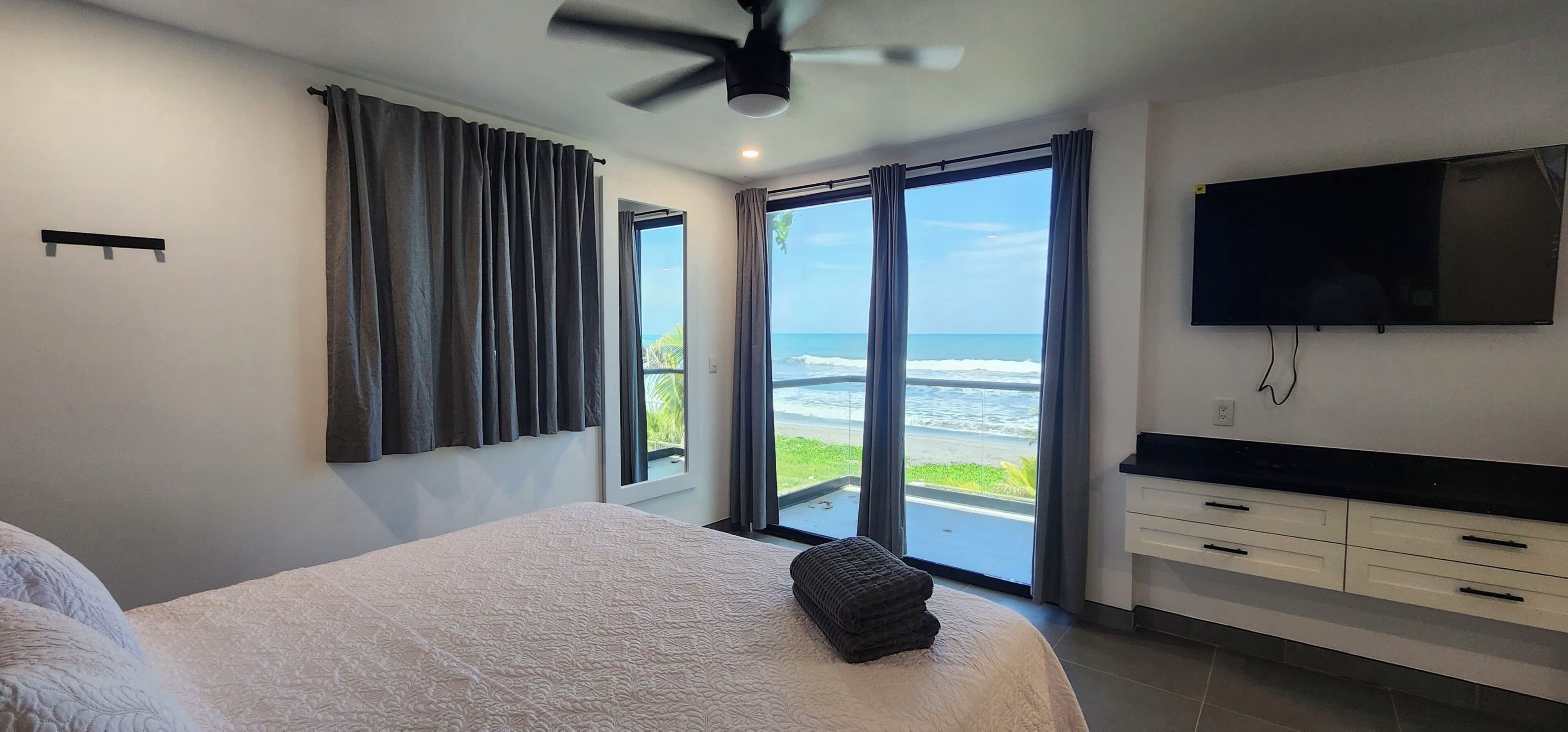 Een slaapkamer met een bed, een televisie, een plafondventilator en uitzicht op de oceaan.