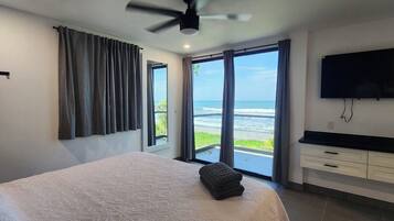 Een slaapkamer met een bed, een televisie, een plafondventilator en uitzicht op de oceaan.