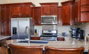 A kitchen with wooden cabinets, a stainless steel refrigerator, a microwave, a stove, and a coffee maker.