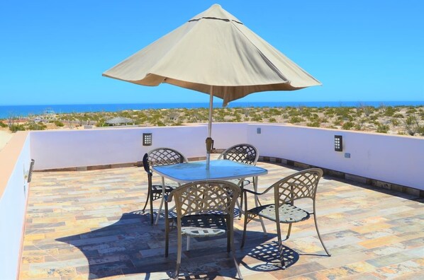 A patio with a table and chairs, an umbrella, and a view of the sea.