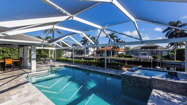 Piscina con struttura in vetro, circondata da palme e vista su una zona residenziale.