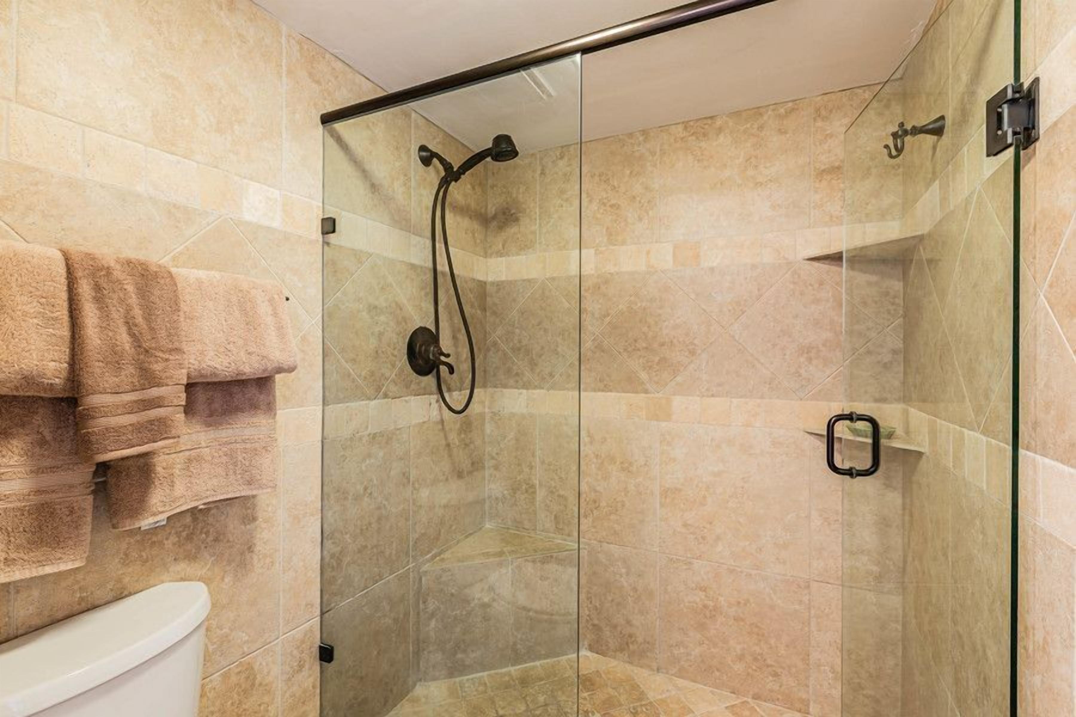 A glass-enclosed shower with beige tiles, a glass door, and a towel rack with folded towels.
