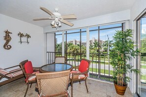 Ein Balkon mit Korbmöbeln, einem Deckenventilator und einem großen Fenster mit Blick auf Gebäude und Grünflächen.
