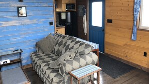 A compact living space with a sofa, a small table, a kitchenette, and a door with a curtain.