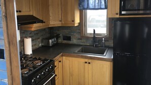 A compact kitchen with wooden cabinets, a gas stove, a toaster, a sink, and a black refrigerator.
