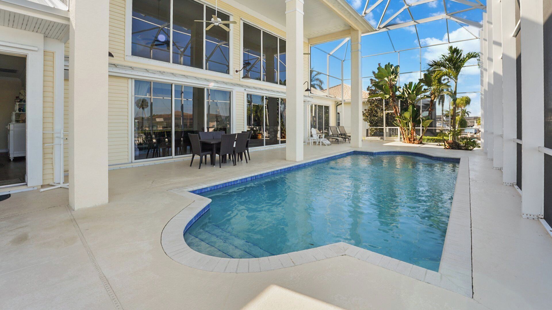 Une piscine intérieure dotée d’un toit en verre, entourée de chaises longues et d’un espace repas avec tables et chaises.