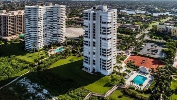 Un immeuble résidentiel de grande hauteur, doté de nombreux balcons, entouré d’une végétation luxuriante et agrémenté d’une piscine.