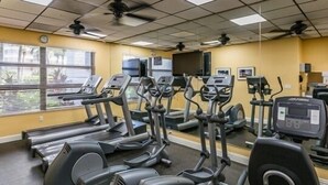 Une salle de sport équipée de plusieurs tapis de course, de plusieurs appareils elliptiques et dotée d’un mur entièrement recouvert de miroirs.