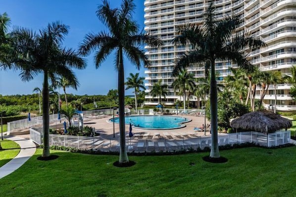 A hotel with a swimming pool surrounded by palm trees and a large building in the background.