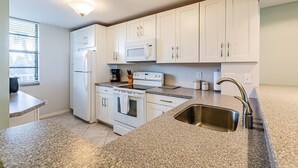 Eine moderne Küche mit weißen Schränken, einer Edelstahl-Spüle, Granit-Arbeitsplatten, einem Kühlschrank, einer Mikrowelle und einem Herd.