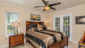 Une chambre avec un grand lit, deux tables de chevet avec des lampes, un ventilateur de plafond et une vue sur l’extérieur, visible à travers une porte vitrée.