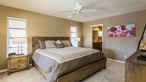 Une chambre à coucher avec un grand lit, un ventilateur de plafond, une table de chevet et une commode.