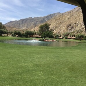 A golf course with a pond, trees, and a mountain backdrop.
