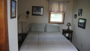 Ein Schlafzimmer mit Bett, Nachttisch, Lampe und einem Fenster mit Vorhang.
