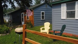 Ein Wohnhaus mit Holzzaun, Grill und zwei Adirondack-Stühlen.