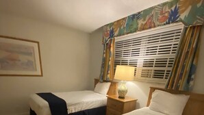 Una habitación de hotel con dos camas, una mesita de noche, una lámpara y una ventana con persianas.