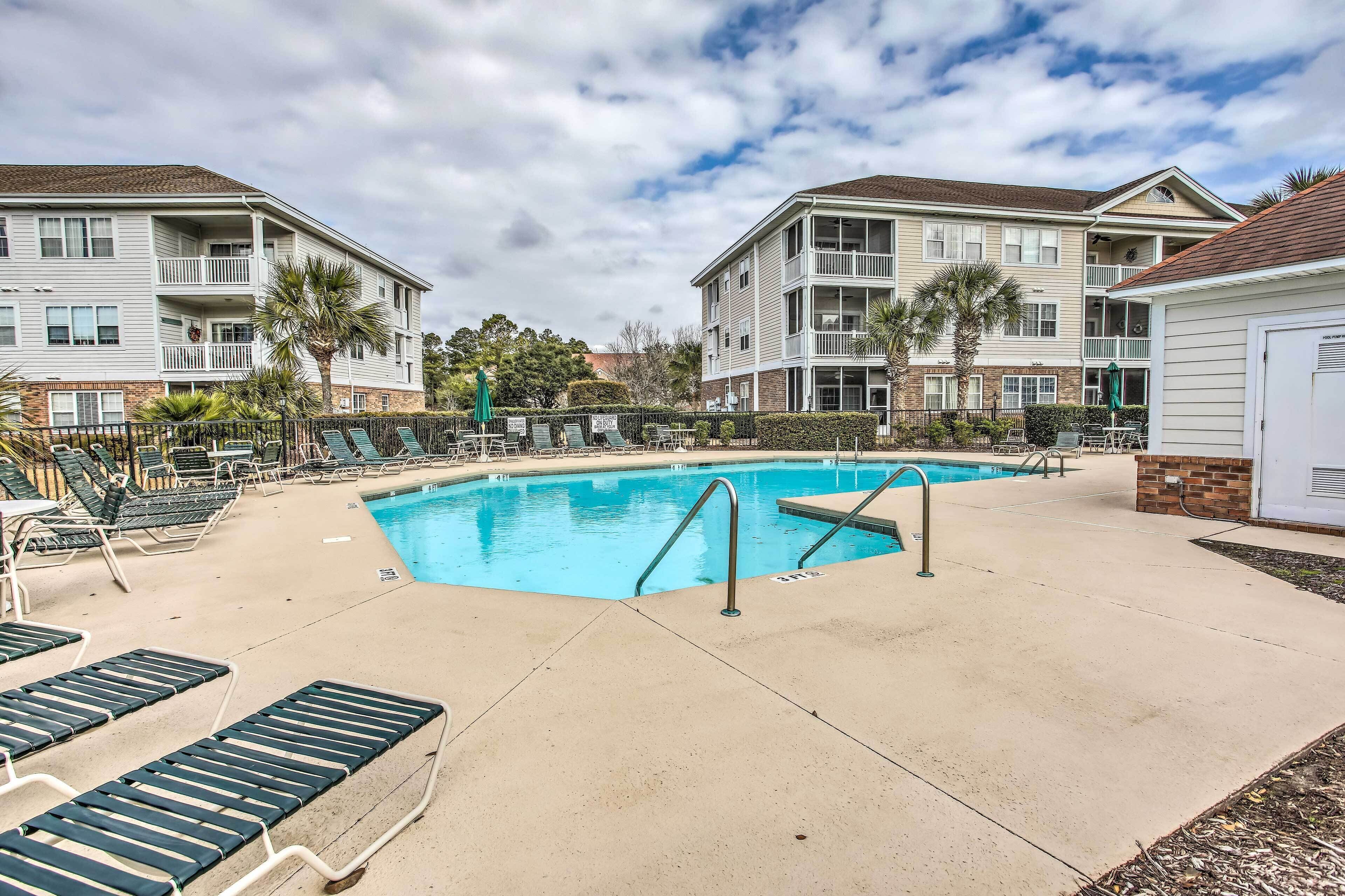 A swimming pool area with lounge chairs and a building with balconies.