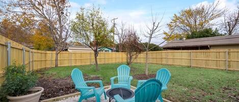 A backyard with a patio area featuring four green Adirondack chairs and a small round table.