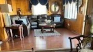 Un comedor con una mesa de madera dispuesta para dos personas, un sofá y un televisor al fondo.