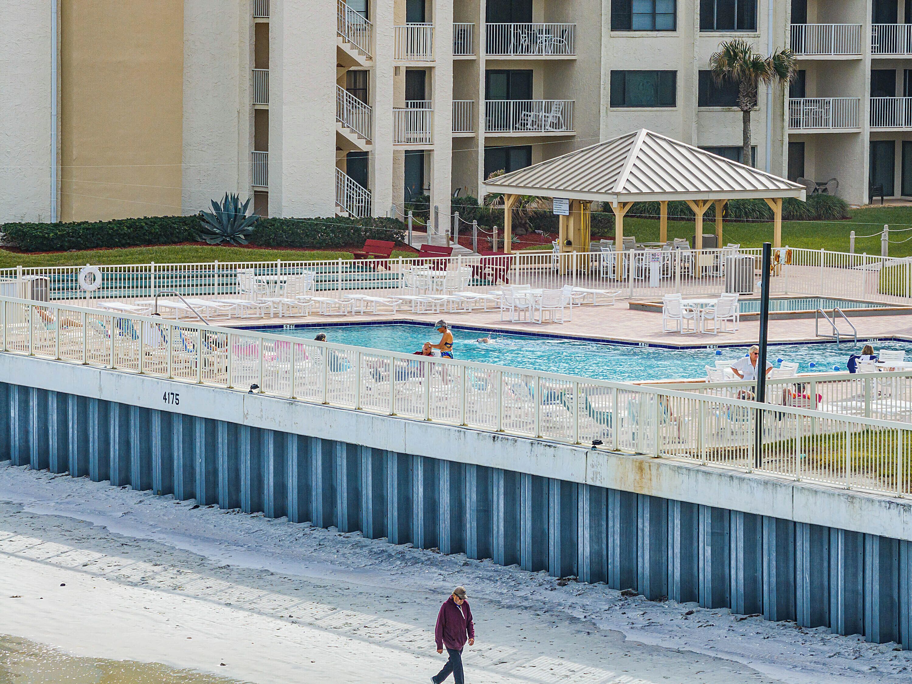 A swimming pool with a fenced deck, lounge chairs, and a gazebo.