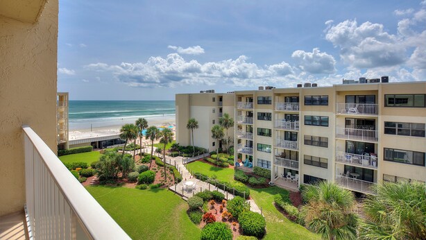 A hotel with multiple balconies overlooking a beach, a well-maintained garden, and a clear view of the ocean.