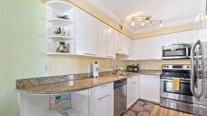 A modern kitchen with white cabinets, granite countertops, stainless steel appliances, and a built-in shelf with decorative items.