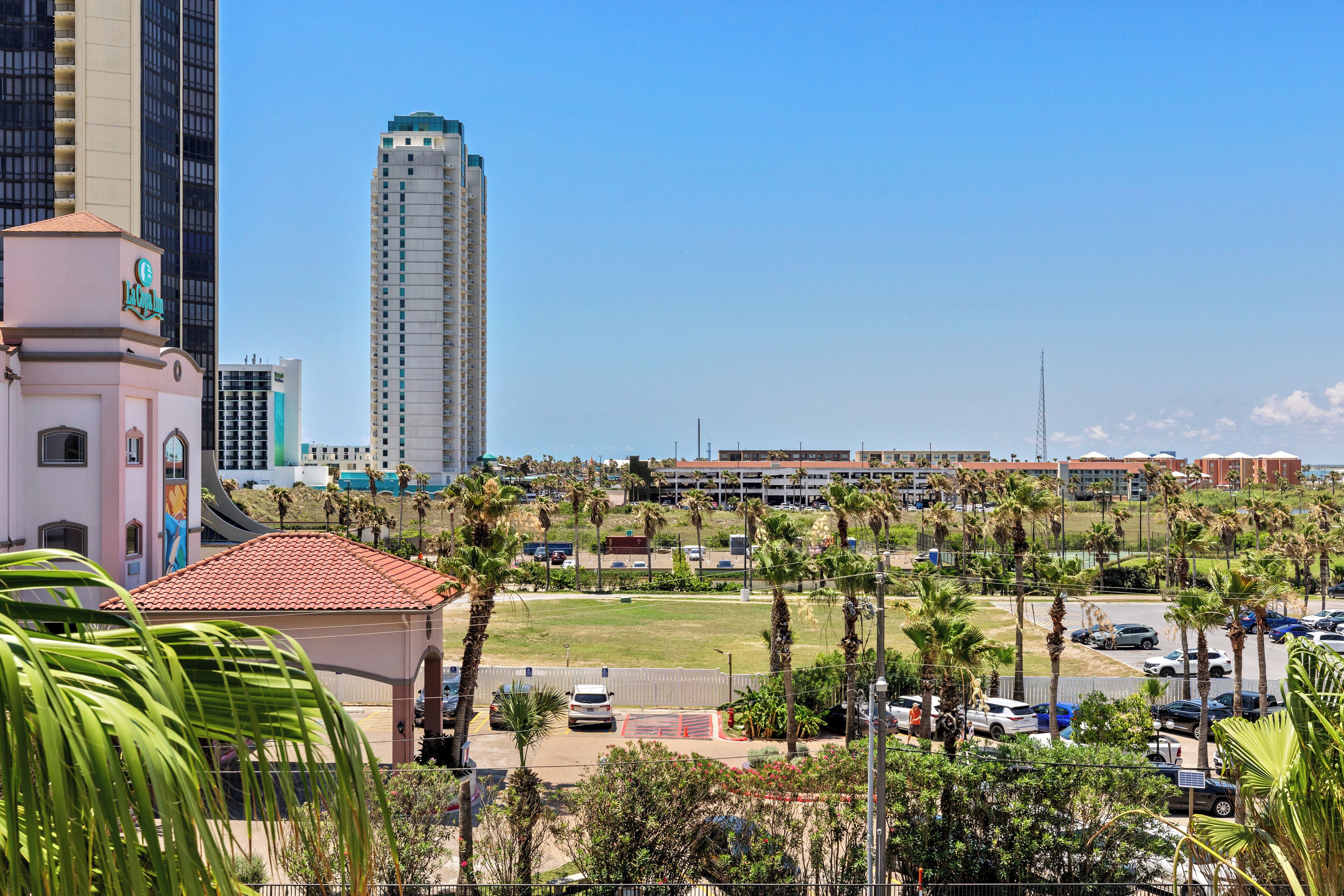 A hotel with a red-tiled roof, a large parking lot, and several palm trees.