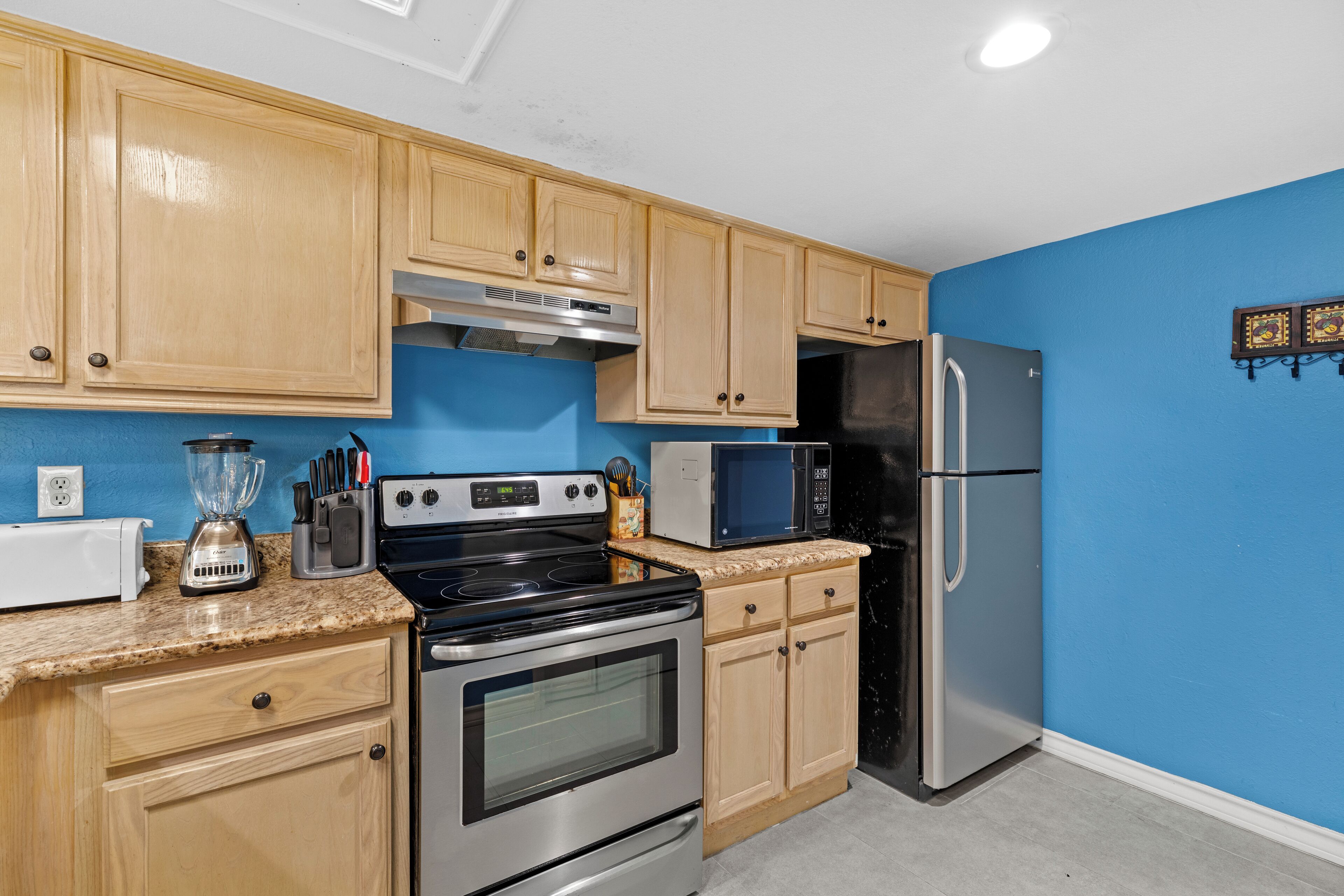 Una cocina con gabinetes de madera, estufa de acero inoxidable, microondas y refrigerador.