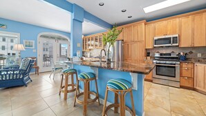 A modern kitchen with wooden cabinets, a stainless steel refrigerator, and a central island with stools. - MY FRIEND'S PLACE EAST - COSTAL COTTAGE, GULF VIEWS FROM DECK, SUPER COZY (Gulf Shores)