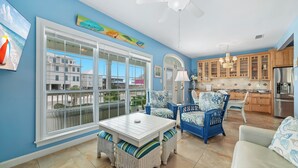 A bright room with a large window, wicker furniture, and a kitchen area. - MY FRIEND'S PLACE EAST - COSTAL COTTAGE, GULF VIEWS FROM DECK, SUPER COZY (Gulf Shores)