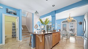 A kitchen with a central island, a dining area with a table and chairs, a staircase, and a bathroom with a toilet and shower. - MY FRIEND'S PLACE EAST - COSTAL COTTAGE, GULF VIEWS FROM DECK, SUPER COZY (Gulf Shores)