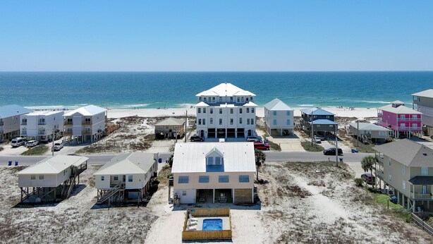 Une propriété située en bord de mer, comprenant plusieurs bâtiments, une plage de sable et l’océan en toile de fond.