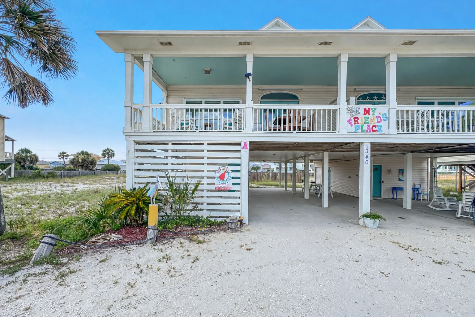 A beachfront property with a covered porch, a sign reading 'My Friends Place', and a sandy driveway.