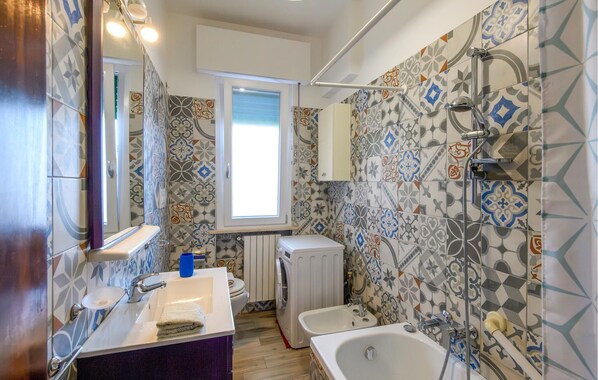 Un baño con baldosas estampadas, un lavabo, un espejo, una ventana, un inodoro, una lavadora y una bañera.