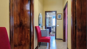 Un couloir avec des portes en bois, une chaise rouge, un miroir et une salle de bain visible au fond.