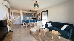 Un saló modern amb un sofà blau fosc, una taula de centre i una zona menjador amb tamborets.
