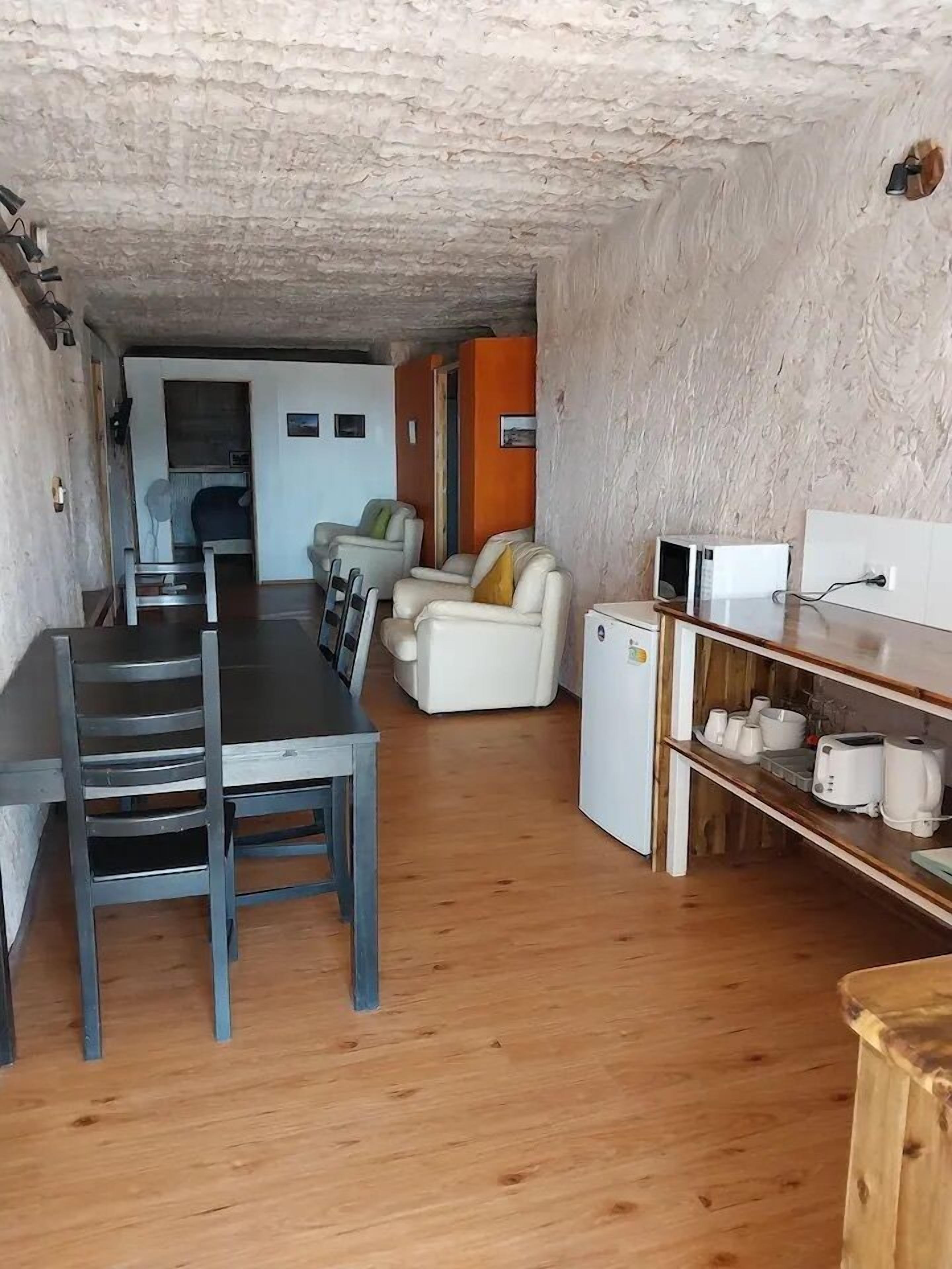 Ett kompakt bostadsutrymme med en matplats, ett litet pentry och en sittgrupp med soffa och fåtöljer.