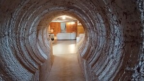 Ein tunnelartiger Innenraum, der in einen modernen Küchenbereich mit weißen Geräten und Holzschränken führt.