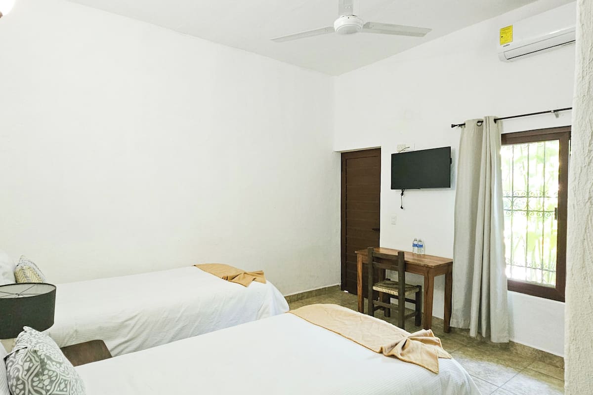 Una habitación con dos camas, un escritorio, una silla, un televisor y una ventana con cortinas.