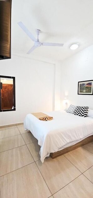 A bedroom with a bed, a ceiling fan, a wall-mounted TV, and a framed picture.