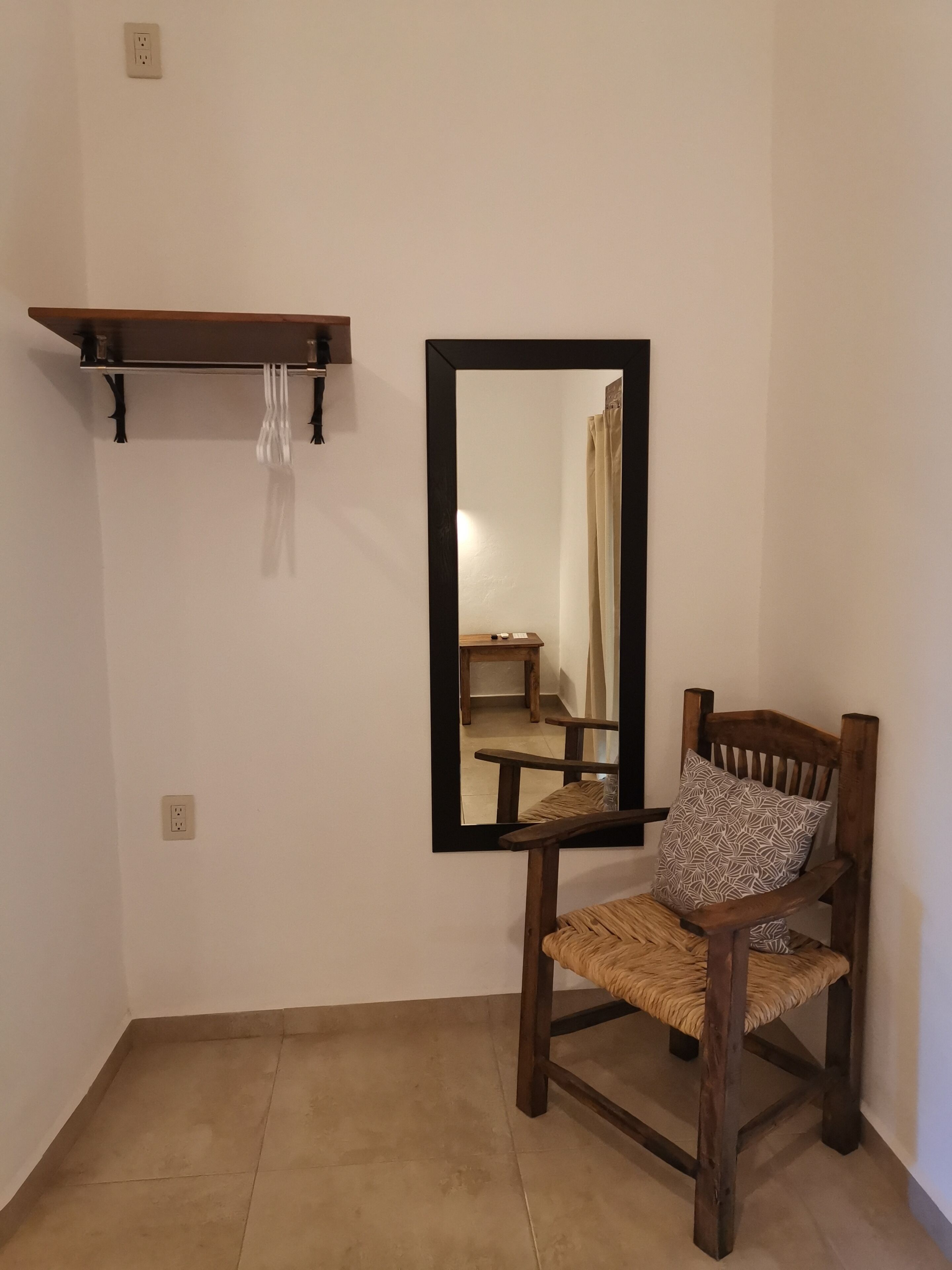 A room with a wooden chair, a mirror, a shelf, and a power outlet.