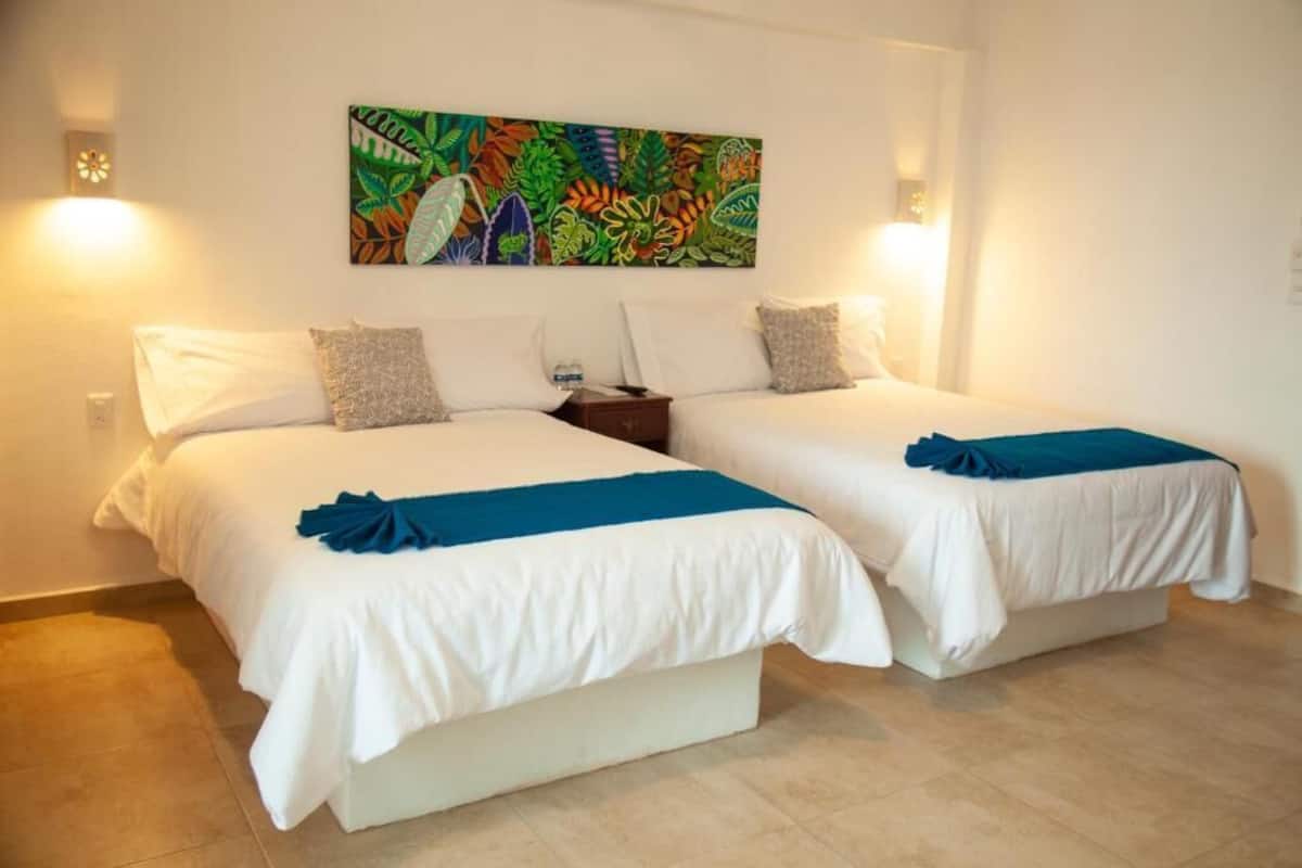 Habitación doble con dos camas, una mesita de noche, un cuadro colgado en la pared y dos lámparas de pared.